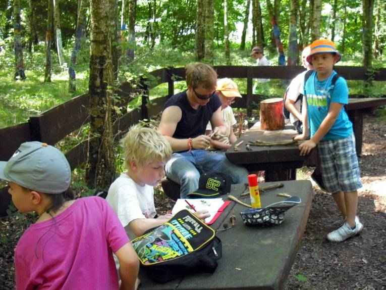 Kinder sitzen im Wald an Tischen