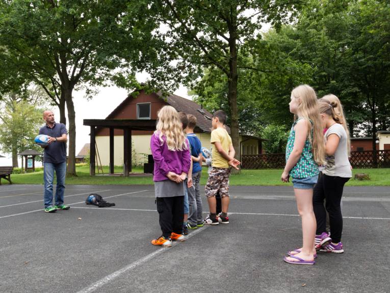 Ein Mann mit einem Rugby-Ei steht vor einer Gruppe mit Kindern.