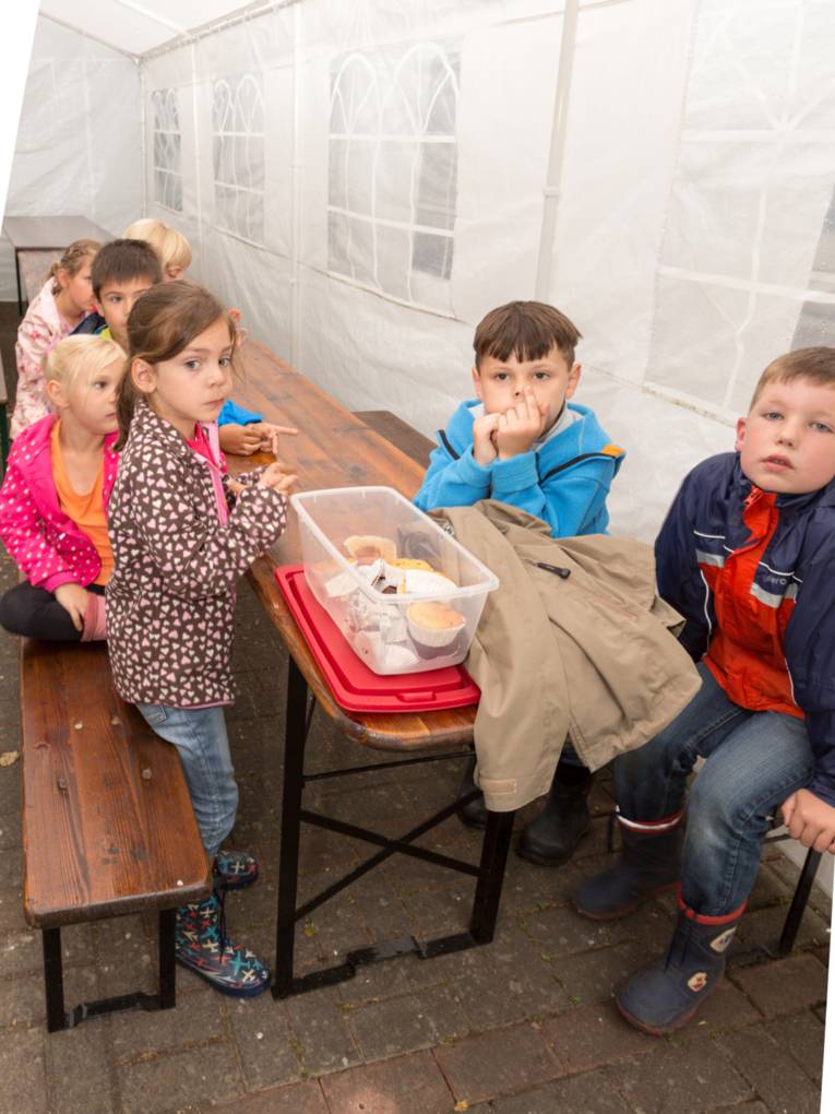 Kinder sitzen in einem Partyzelt und essen Muffins.