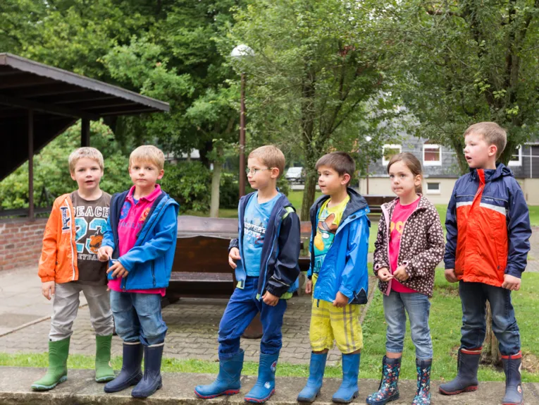 Kinder stehen nebeneinander auf einer Mauer.