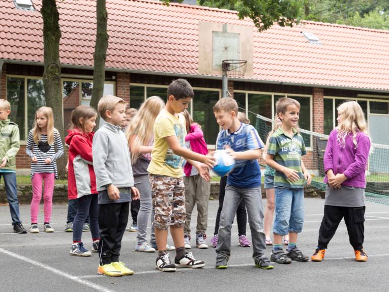 Kinder üben mit einem Rugby-Ei das Pässe werfen.