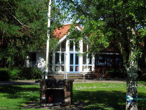 Gebäudeeingang mit Bäumen und Wiese davor. Auf der Wiese ist ein gemauerter Grill. Gebäudeeingang mit Bäumen und Wiese davor. Auf der Wiese ist ein gemauerter Grill.